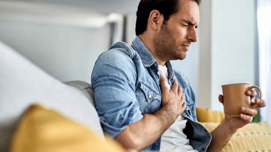 young-man-feeling-sick-holding-his-chest-pain-while-drinking-tea-living-room
